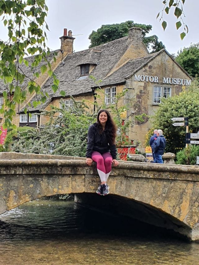 Abi-sits-on-stone-bench-outside-motor-museum-in-Cotswolds-village